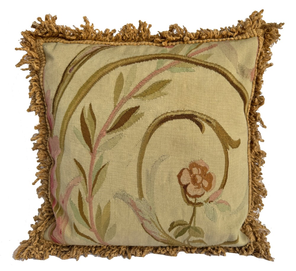 A square antique Aubusson tapestry cushion featuring scrolling floral motifs in muted green and pink on a cream background, finished with an ochre fringed border.