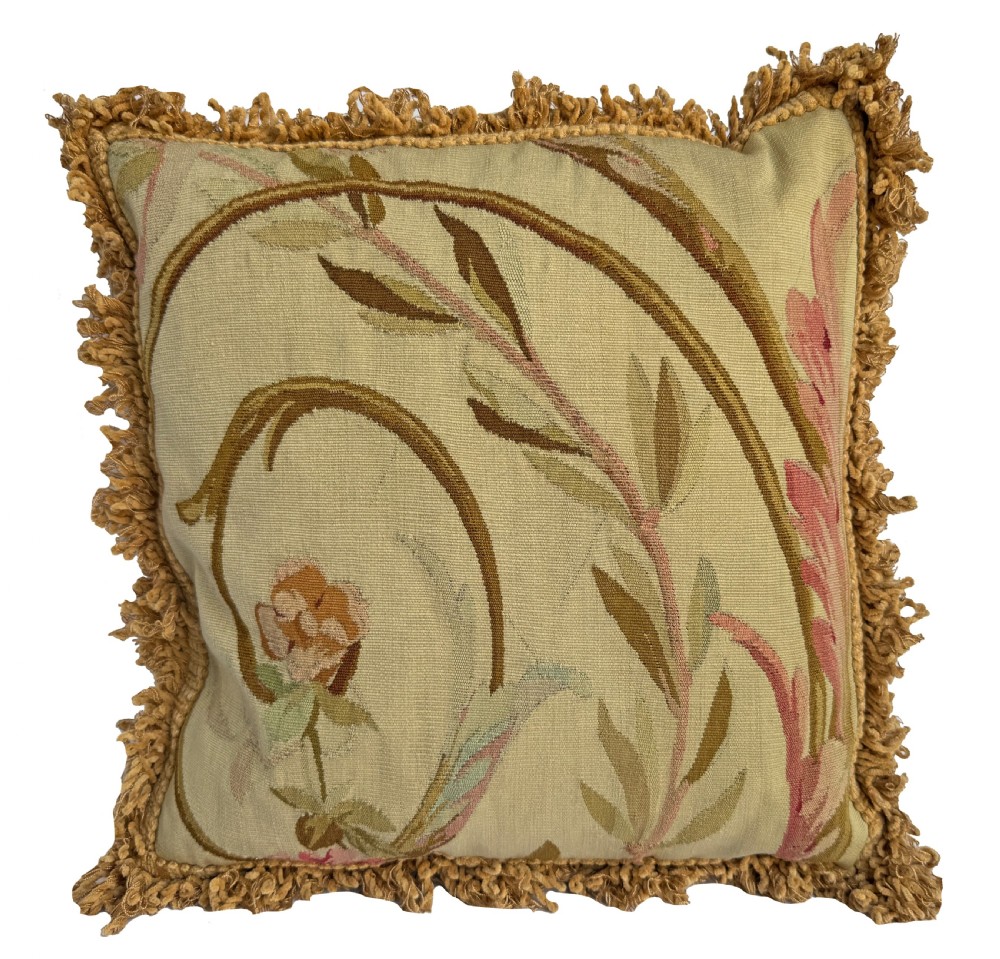 A square antique woven tapestry cushion featuring botanical scrolls in soft pink and green tones, trimmed with a beige looped fringe.