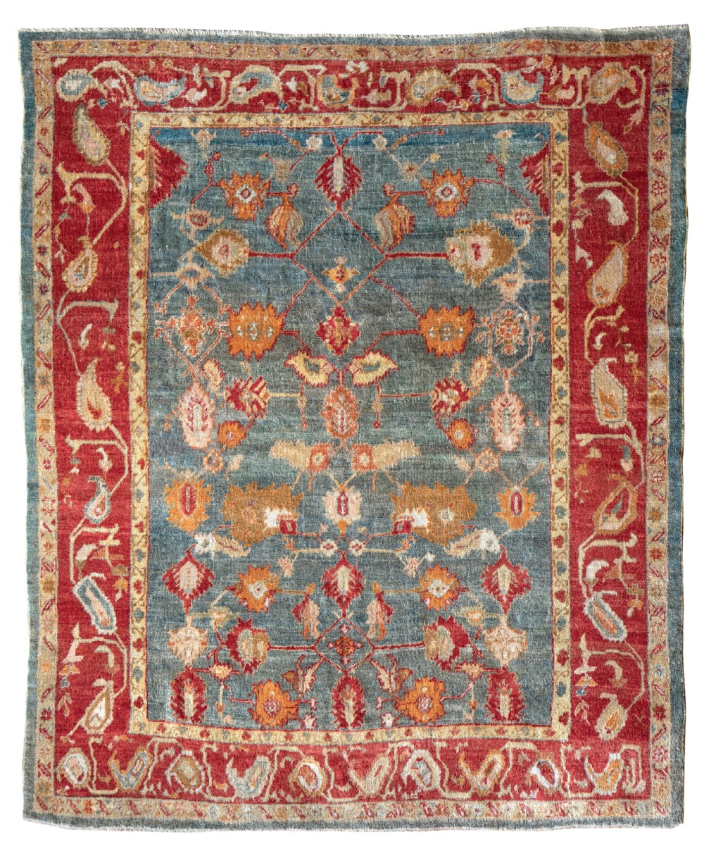 A hand-knotted antique textile rug featuring a slate blue central field decorated with terracotta palmettes and framed by a wide red paisley border.
