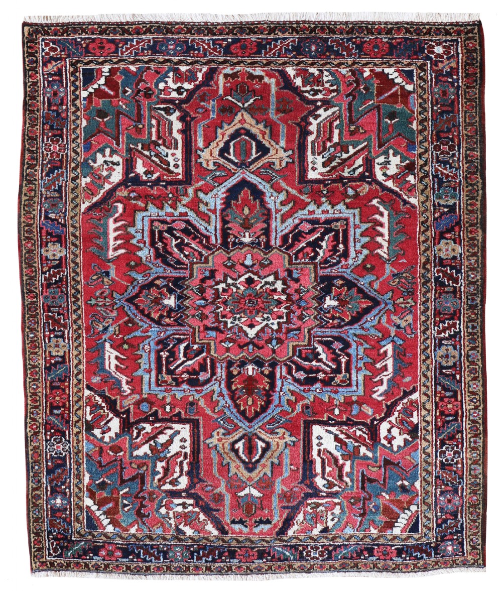 An antique Persian Heriz wool rug featuring a large central geometric medallion in red, blue, and ivory tones against a rich red field.