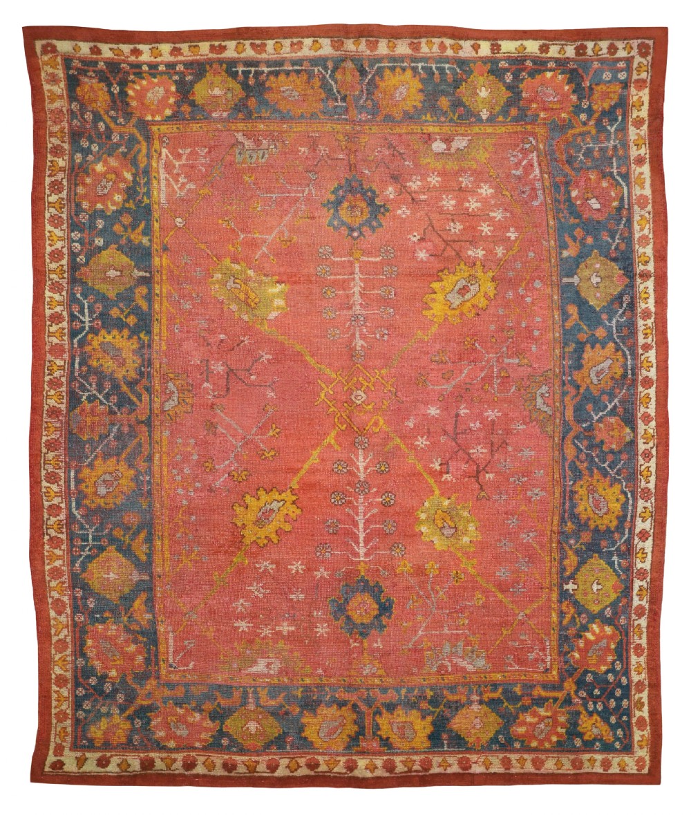 An antique Turkish Ushak wool carpet featuring a muted terracotta field decorated with central stylized floral motifs and framed by a deep blue patterned border.