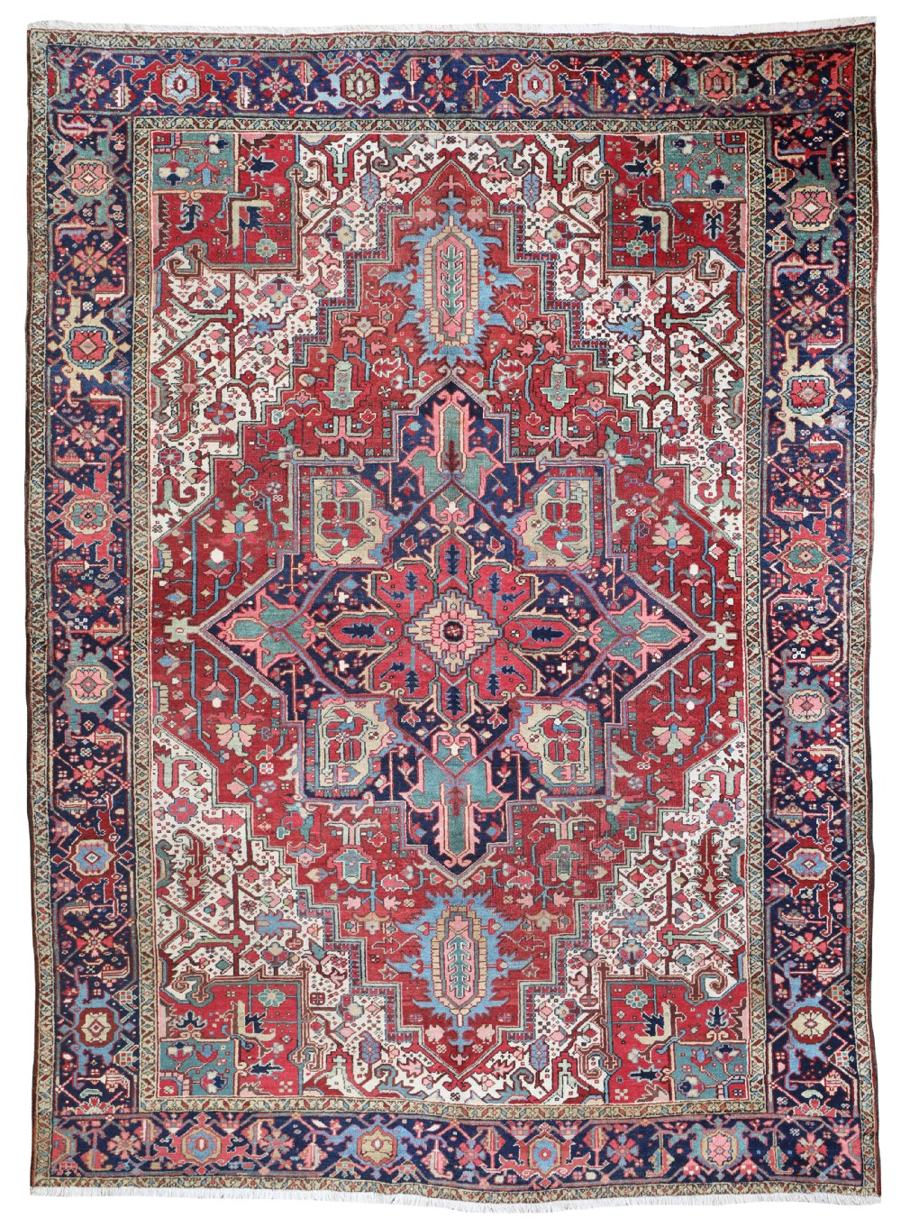 A large hand-knotted antique Heriz wool carpet featuring a geometric central medallion in navy blue, sky blue, and terracotta red on an ivory field.