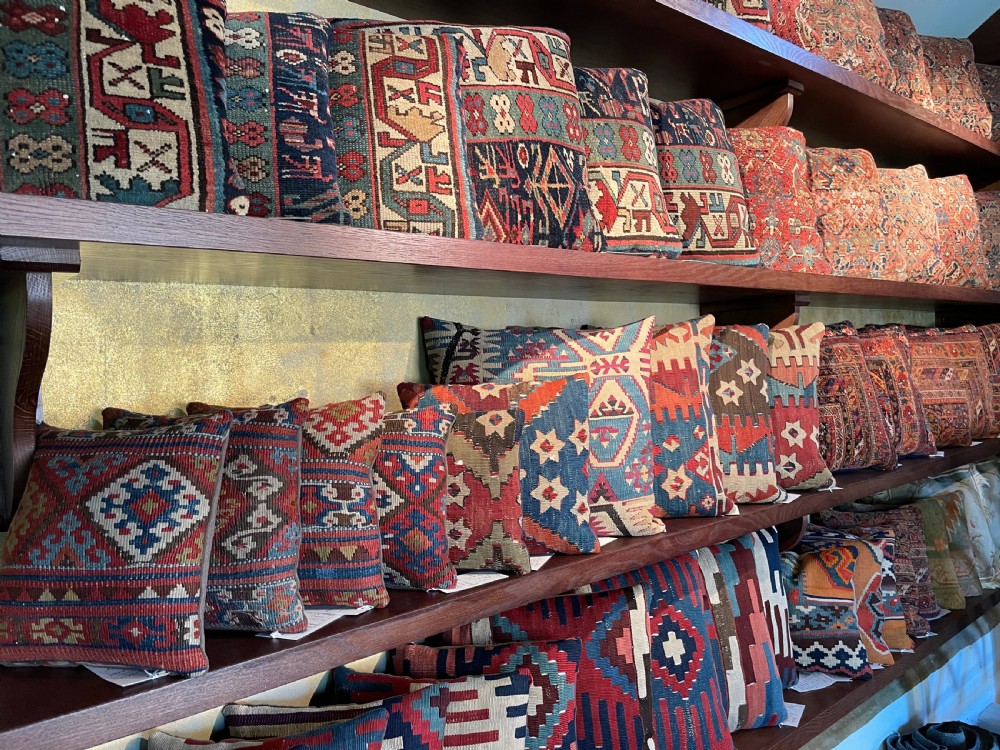 A square flat-weave wool kilim cushion featuring geometric diamond and cross motifs in terracotta red, blue, sage green, and dark brown. View VII