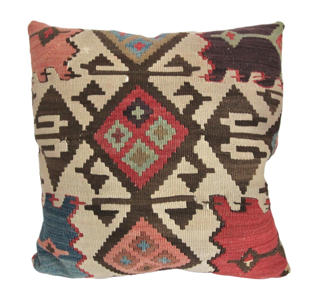 A square cushion crafted from flat-woven kilim rug textile featuring diamond and geometric motifs in brown, red, blue, and cream wool.
