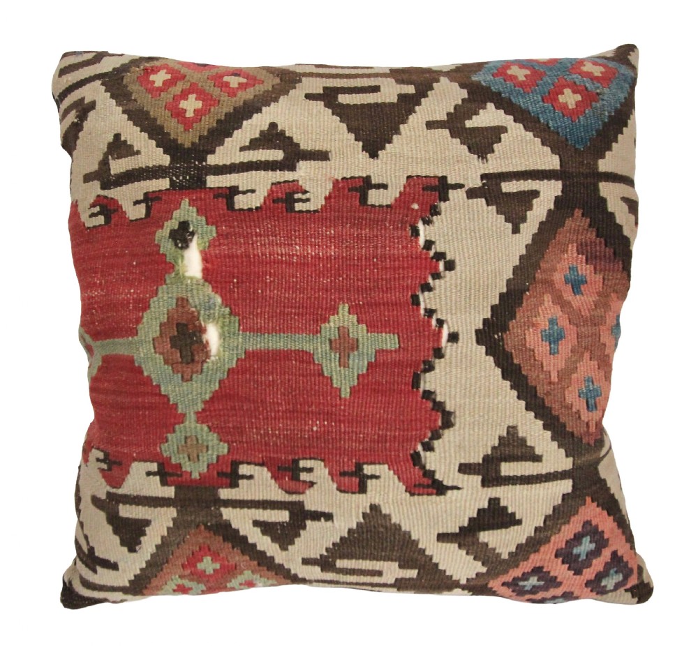 A square antique wool kilim cushion with handwoven geometric diamond and latchhook patterns in red, cream, dark brown, and teal.