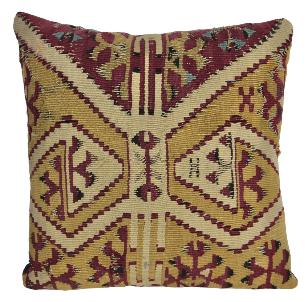 A square cushion made from handwoven kilim textile featuring geometric diamond motifs in ochre yellow, burgundy red, and beige.