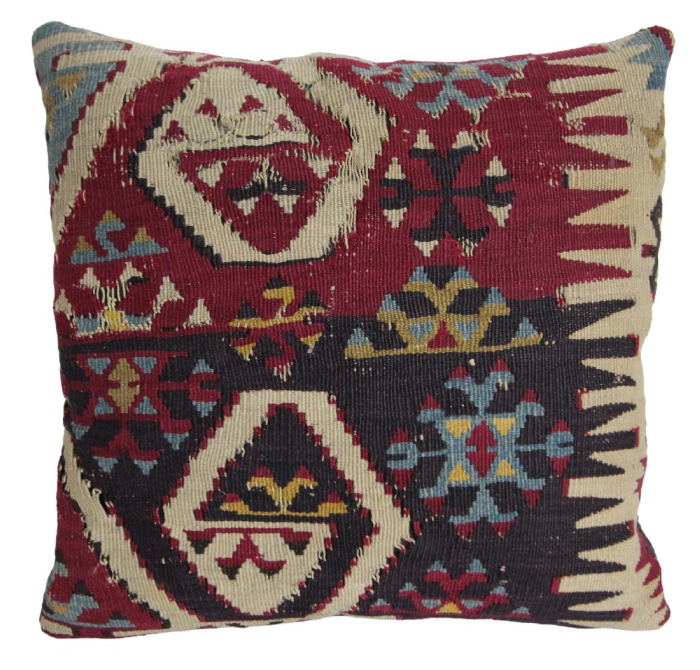 A square handwoven antique kilim cushion featuring geometric Anatolian tribal motifs woven in deep red, cream, navy blue, and ochre wool.