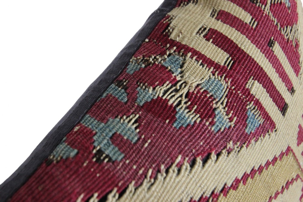 A square cushion crafted from flat-woven wool featuring geometric tribal motifs in beige, burgundy red, and dark blue hues. View II