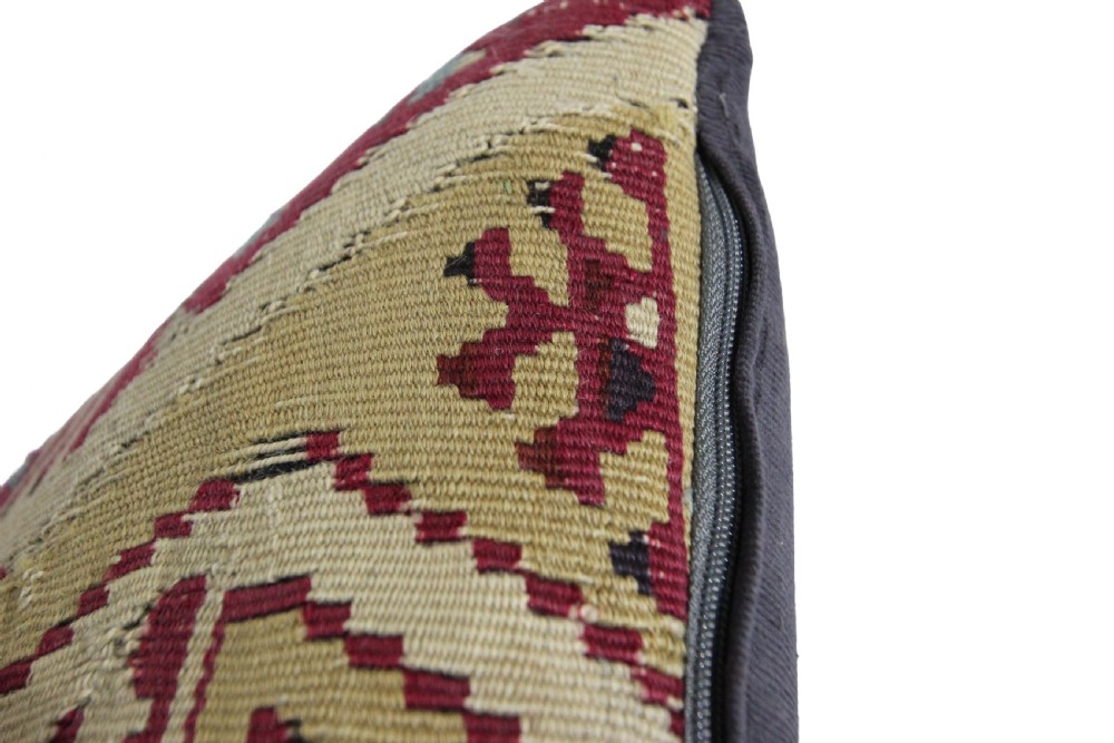 A square cushion crafted from flat-woven wool featuring geometric tribal motifs in beige, burgundy red, and dark blue hues. View III