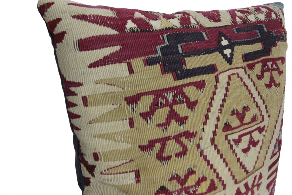 A square cushion crafted from flat-woven wool featuring geometric tribal motifs in beige, burgundy red, and dark blue hues. View VIII