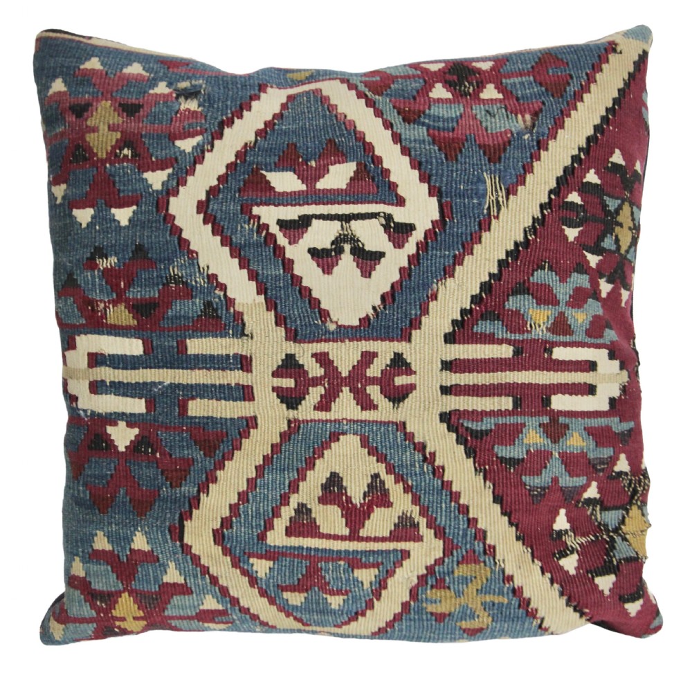 A square flatwoven kilim cushion featuring geometric diamond motifs in blue, burgundy, cream, and yellow wool threads.