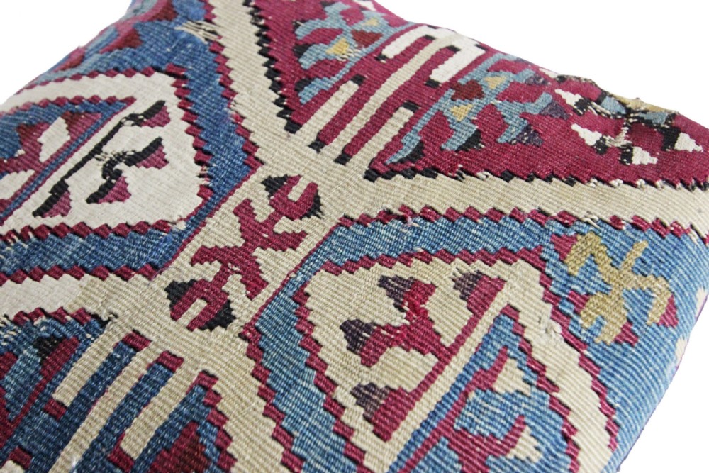 A square flatwoven kilim cushion featuring geometric diamond motifs in blue, burgundy, cream, and yellow wool threads. View V