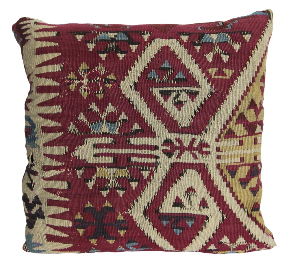 A square scatter cushion crafted from a hand-woven kilim textile in deep crimson red, cream, and soft blue geometric patterns.
