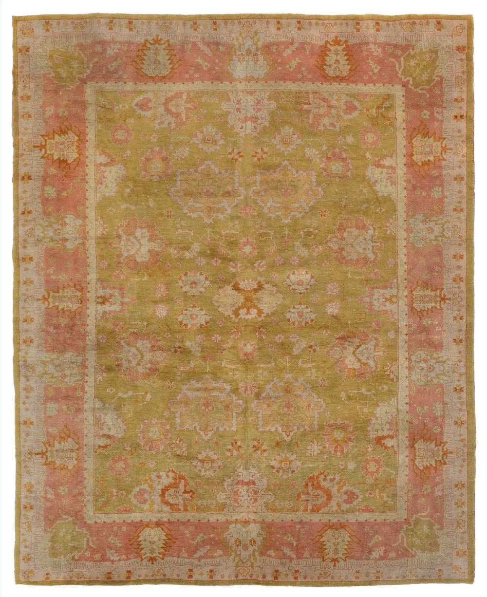A hand-knotted antique Ushak wool carpet featuring an olive green central field decorated with muted botanical medallions and framed by a terracotta pink floral border.