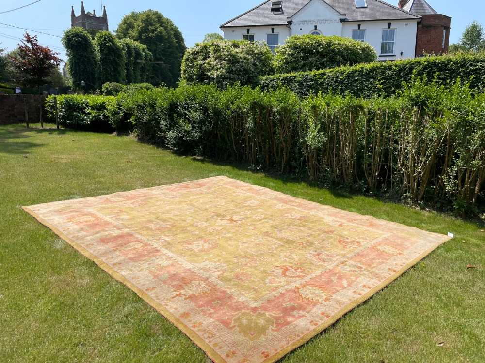 A hand-knotted antique Ushak wool carpet featuring an olive green central field decorated with muted botanical medallions and framed by a terracotta pink floral border. View X