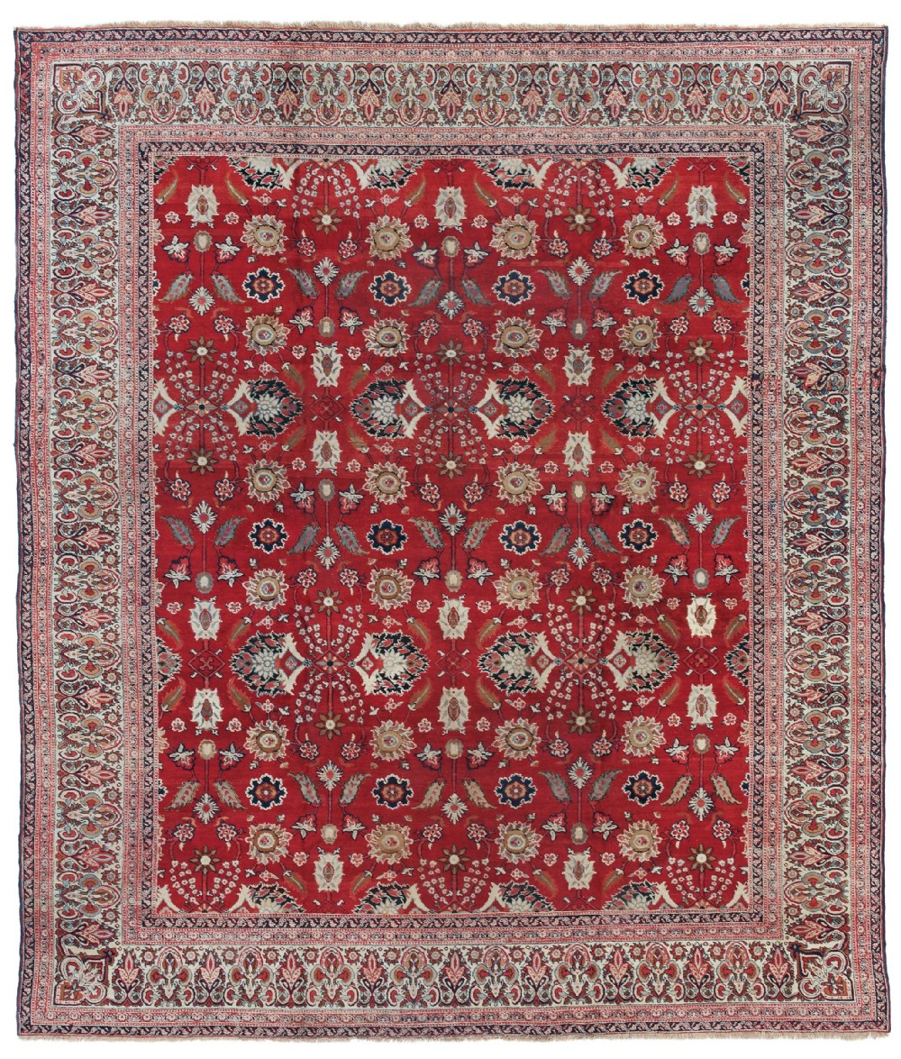 An antique Agra carpet featuring a vibrant red field adorned with intricate allover floral motifs framed by a wide ivory and navy multi-band border.