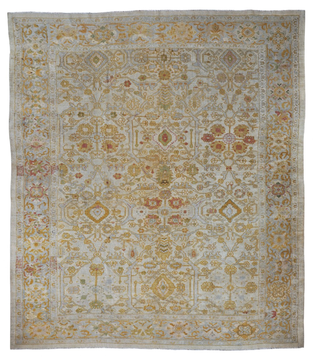 A large rectangular antique Ziegler carpet featuring a cream ground with intricate muted ochre, terracotta, and soft blue floral motifs framed by a wide border.