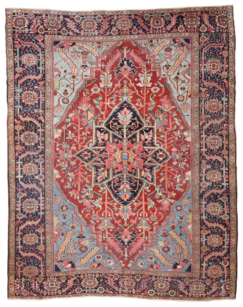 An antique hand-knotted Heriz wool carpet featuring a large geometric star medallion in terracotta red and navy blue framed by light blue spandrels and a dark decorative border.