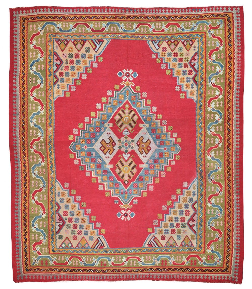 A flatwoven Anatolian kilim rug with a vibrant red field, central diamond medallion, and stepped geometric borders in green, sky blue, and cream.
