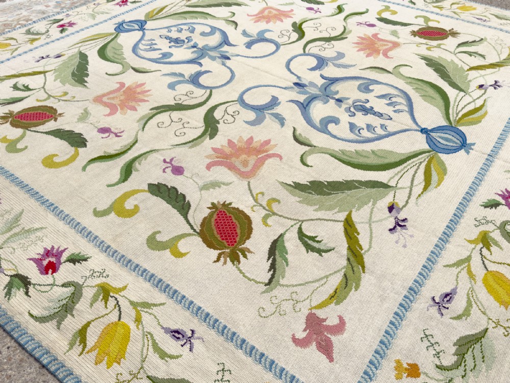 A square cream wool needlepoint rug featuring intricate green botanical scrollwork, pink blossoms, and pomegranate motifs within a decorative floral border. View II