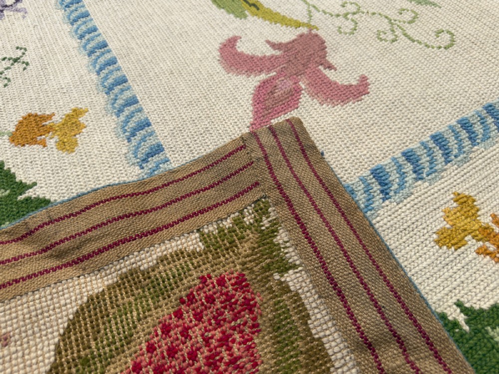 A square cream wool needlepoint rug featuring intricate green botanical scrollwork, pink blossoms, and pomegranate motifs within a decorative floral border. View III