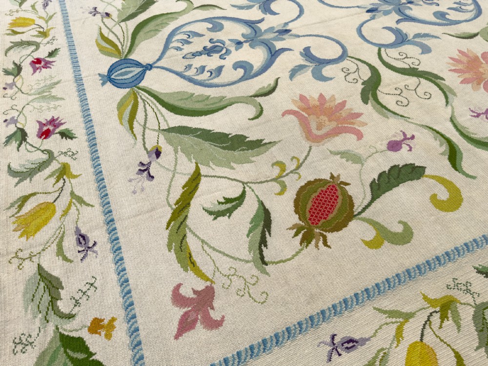 A square cream wool needlepoint rug featuring intricate green botanical scrollwork, pink blossoms, and pomegranate motifs within a decorative floral border. View IV