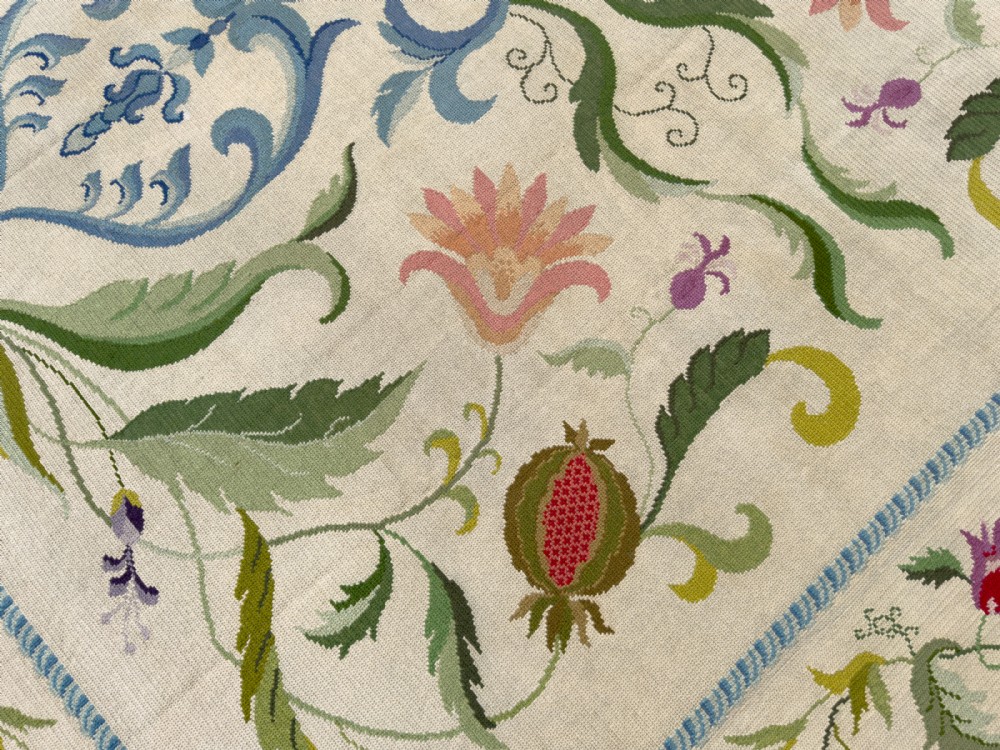 A square cream wool needlepoint rug featuring intricate green botanical scrollwork, pink blossoms, and pomegranate motifs within a decorative floral border. View V