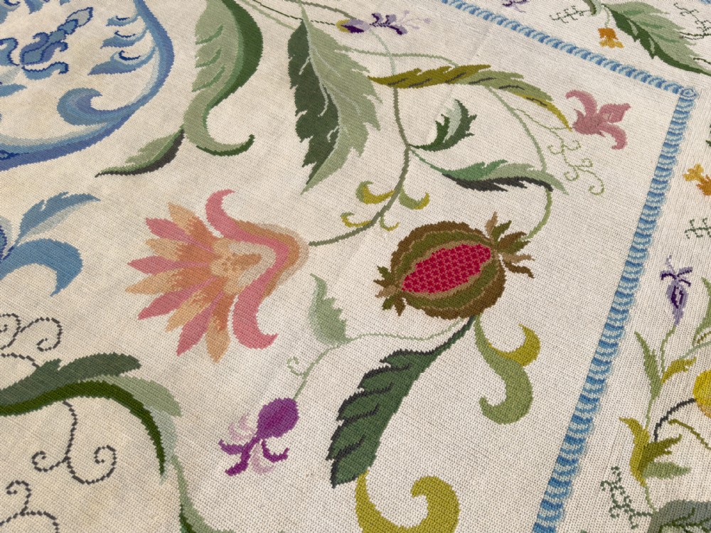 A square cream wool needlepoint rug featuring intricate green botanical scrollwork, pink blossoms, and pomegranate motifs within a decorative floral border. View VI