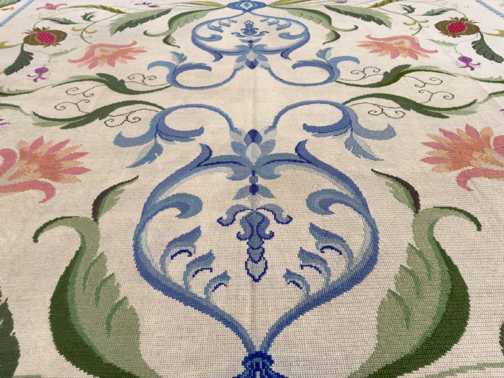 A square cream wool needlepoint rug featuring intricate green botanical scrollwork, pink blossoms, and pomegranate motifs within a decorative floral border. View VIII