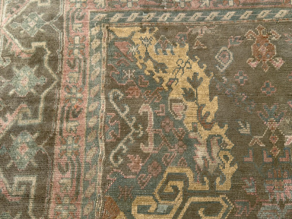 An antique hand-knotted Ushak wool carpet featuring a muted grey-green field adorned with central medallions, floral motifs, and multi-layered geometric borders in soft terracotta, pink, and gold tones. View II