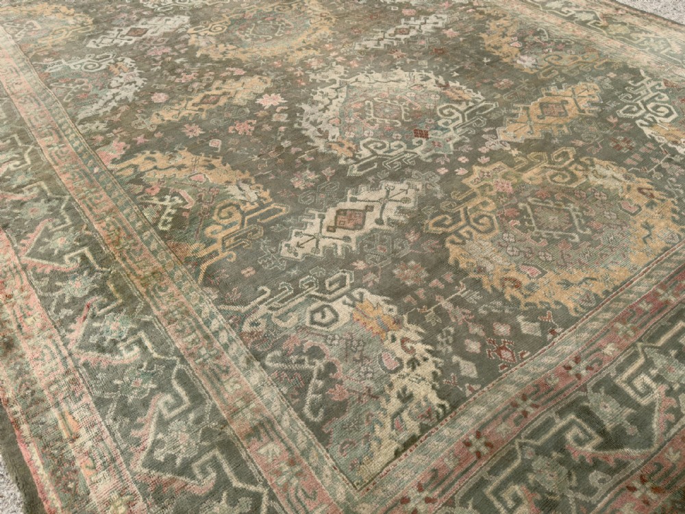 An antique hand-knotted Ushak wool carpet featuring a muted grey-green field adorned with central medallions, floral motifs, and multi-layered geometric borders in soft terracotta, pink, and gold tones. View III