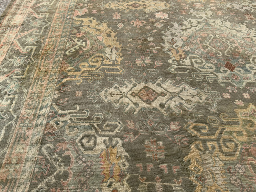 An antique hand-knotted Ushak wool carpet featuring a muted grey-green field adorned with central medallions, floral motifs, and multi-layered geometric borders in soft terracotta, pink, and gold tones. View IV