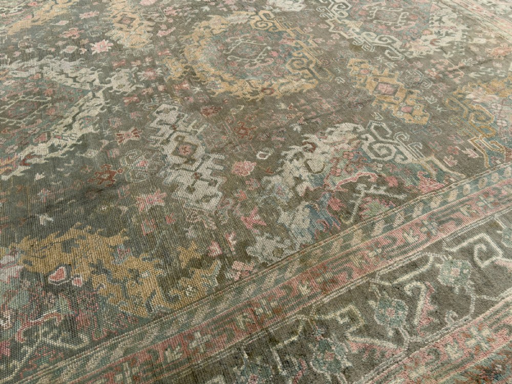 An antique hand-knotted Ushak wool carpet featuring a muted grey-green field adorned with central medallions, floral motifs, and multi-layered geometric borders in soft terracotta, pink, and gold tones. View VI