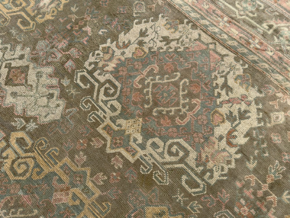 An antique hand-knotted Ushak wool carpet featuring a muted grey-green field adorned with central medallions, floral motifs, and multi-layered geometric borders in soft terracotta, pink, and gold tones. View VII