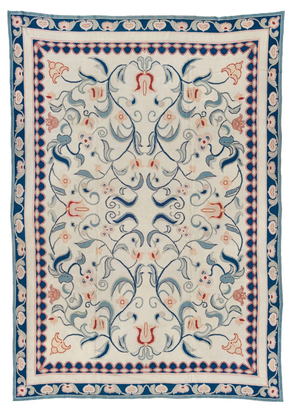 A rectangular Portuguese needlepoint wool rug featuring symmetrical floral scrollwork in blue and terracotta tones against an off-white field.