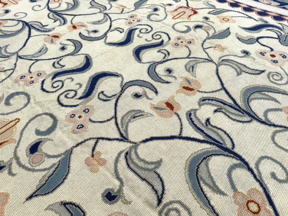 A rectangular Portuguese needlepoint wool rug featuring symmetrical floral scrollwork in blue and terracotta tones against an off-white field. View II