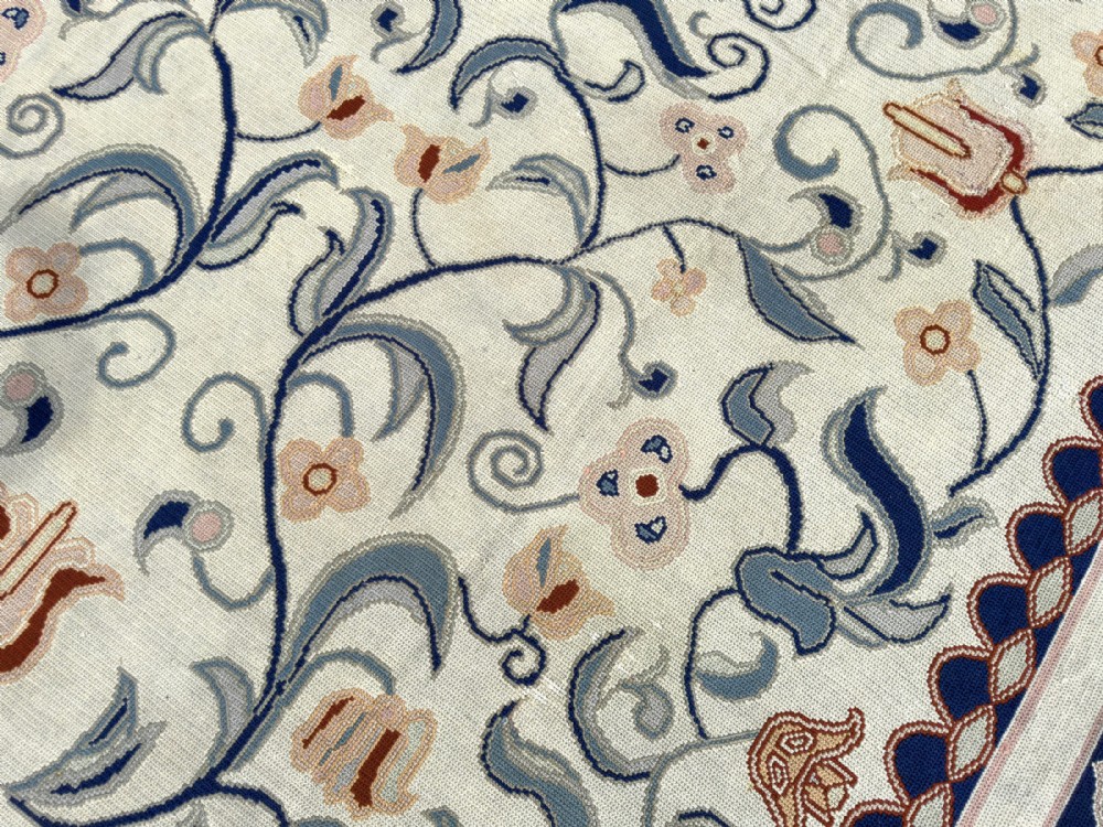 A rectangular Portuguese needlepoint wool rug featuring symmetrical floral scrollwork in blue and terracotta tones against an off-white field. View IV