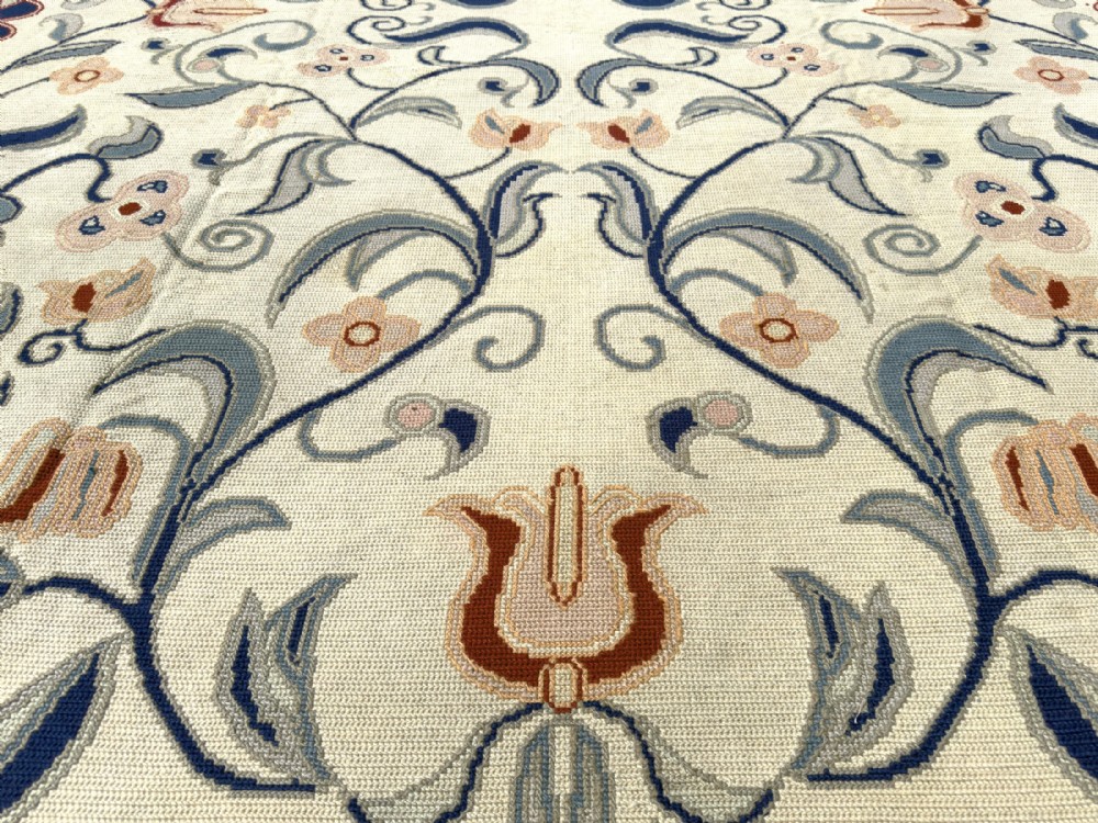 A rectangular Portuguese needlepoint wool rug featuring symmetrical floral scrollwork in blue and terracotta tones against an off-white field. View VI