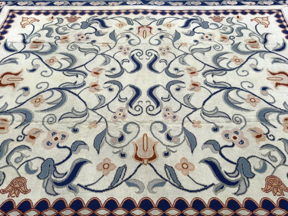 A rectangular Portuguese needlepoint wool rug featuring symmetrical floral scrollwork in blue and terracotta tones against an off-white field. View VIII