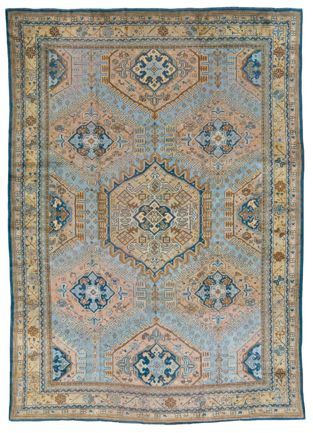 A large hand-knotted antique Ushak wool carpet featuring geometric medallions and intricate borders in soft blue, terracotta, and beige tones.