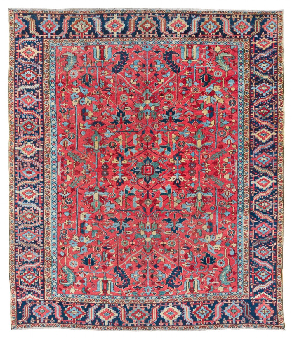 An antique hand-knotted Persian Heriz wool carpet featuring a central geometric medallion, detailed angular floral motifs on a terracotta red field, and a dark navy blue outer border.