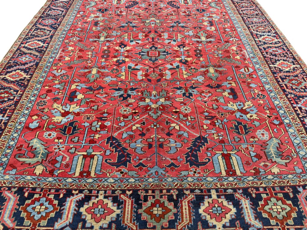 An antique hand-knotted Persian Heriz wool carpet featuring a central geometric medallion, detailed angular floral motifs on a terracotta red field, and a dark navy blue outer border. View II