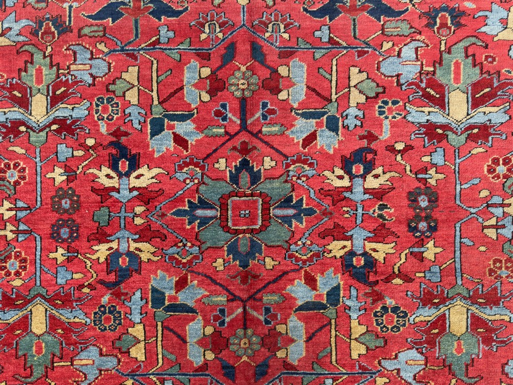 An antique hand-knotted Persian Heriz wool carpet featuring a central geometric medallion, detailed angular floral motifs on a terracotta red field, and a dark navy blue outer border. View VII