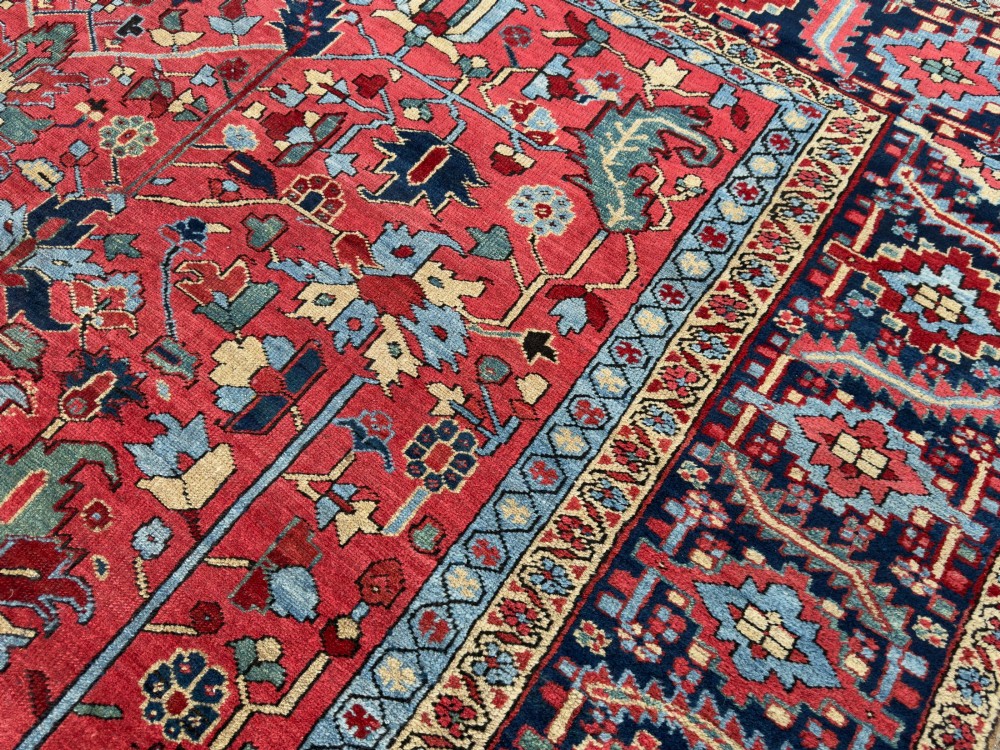 An antique hand-knotted Persian Heriz wool carpet featuring a central geometric medallion, detailed angular floral motifs on a terracotta red field, and a dark navy blue outer border. View VIII