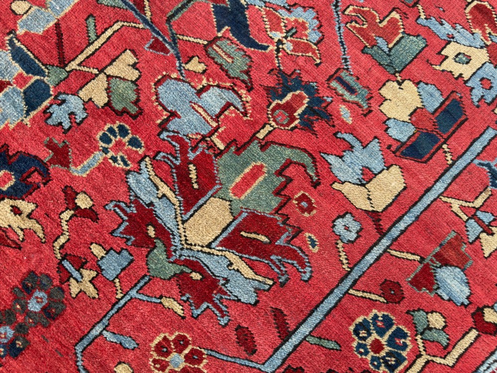 An antique hand-knotted Persian Heriz wool carpet featuring a central geometric medallion, detailed angular floral motifs on a terracotta red field, and a dark navy blue outer border. View IX