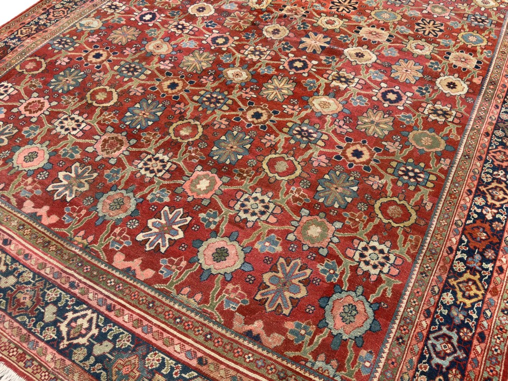 An antique Sultanabad hand-knotted wool carpet featuring an all-over repeating geometric floral pattern on a terracotta red field with a dark blue patterned border. View III