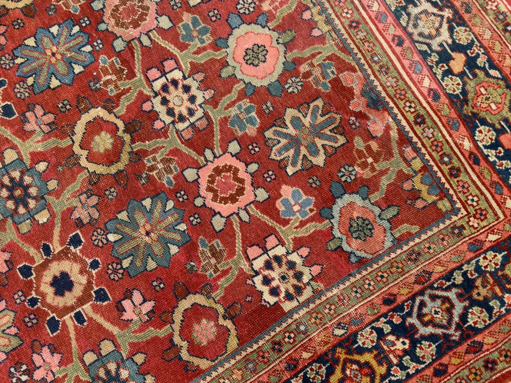 An antique Sultanabad hand-knotted wool carpet featuring an all-over repeating geometric floral pattern on a terracotta red field with a dark blue patterned border. View IV