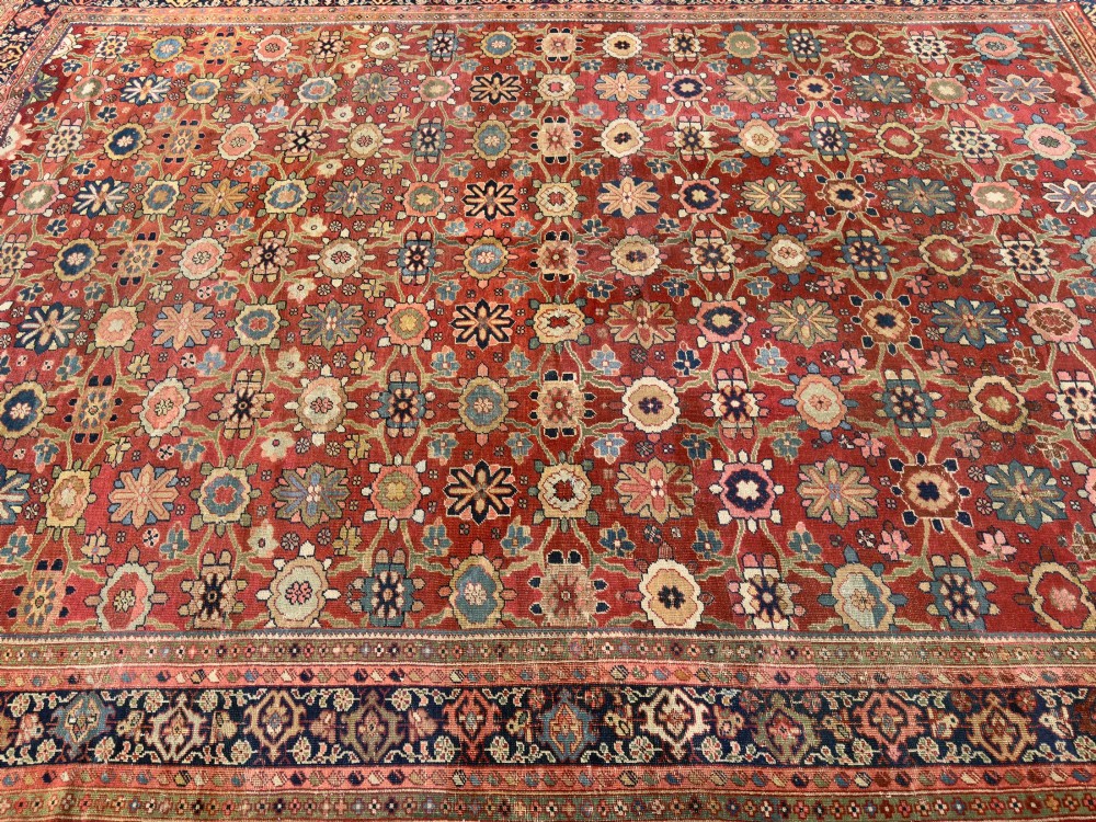 An antique Sultanabad hand-knotted wool carpet featuring an all-over repeating geometric floral pattern on a terracotta red field with a dark blue patterned border. View V
