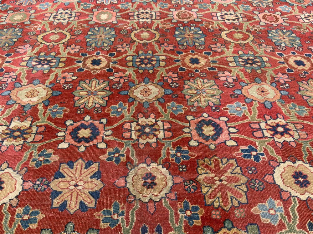 An antique Sultanabad hand-knotted wool carpet featuring an all-over repeating geometric floral pattern on a terracotta red field with a dark blue patterned border. View VI