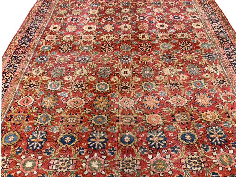 An antique Sultanabad hand-knotted wool carpet featuring an all-over repeating geometric floral pattern on a terracotta red field with a dark blue patterned border. View IX
